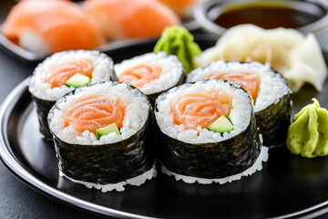Sushi rolls with salmon and cucumber served on a black plate in a dining setting