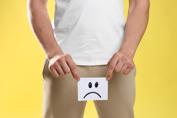 STD (sexually transmitted diseases). Man holding sticky note with drawn sad face on yellow...