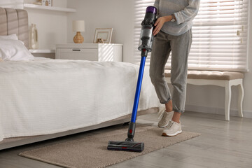 Young woman cleaning floor with cordless vacuum cleaner in bedroom, closeup