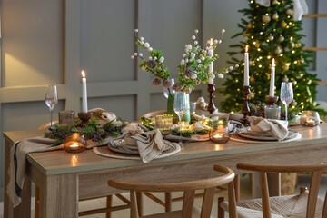 Christmas table setting with stylish dishware, glasses and burning candles in festive decorated room