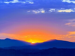 Obraz premium Vibrant Sunset Over Blue Mountains with Radiant Sky