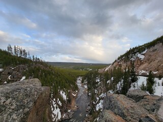 Snowy Canyon Landscape with Pine Forest and River Under Cloudy Sky