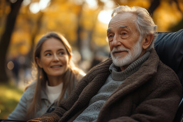 Obraz premium An elderly man in a wheelchair in the foreground smiling, behind sits an elderly woman in a park