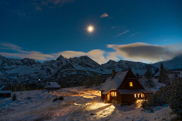 Cozy wooden cottage in snowy mountains, moonlight on the cabin. Winter wonderland