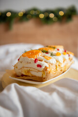 Close-up of delicious Meringue Roll with Orange Curd, layered dessert with oranges, pomegranate seeds, cream on white plate. A festive holiday backdrop with soft fairy lights adds a warm atmosphere.