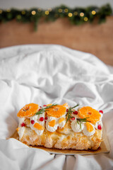 Close-up of delicious Meringue Roll with Orange Curd, layered dessert with oranges, pomegranate seeds, cream on white plate. A festive holiday backdrop with soft fairy lights adds a warm atmosphere.