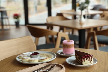 Delicious cottage cheese pancakes, cake and coffee served on wooden table in cafe