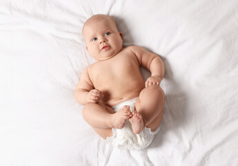 Cute little baby in diaper on bed, top view