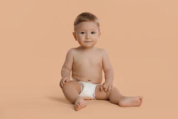 Cute little baby in diaper sitting on beige background