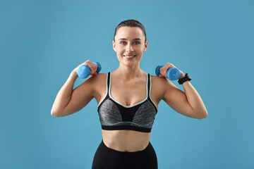 Fototapeta premium Woman in gym clothes exercising with dumbbells on light blue background