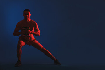 Man exercising with dumbbells in red light on blue background, space for text