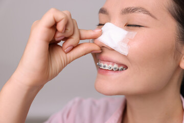 Woman with medical bandage on her nose after plastic surgery operation against light grey background, closeup