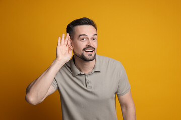 Man showing hand to ear gesture on orange background