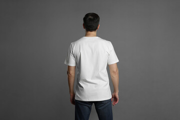 Man in blank white t-shirt on grey background, back view. Mockup for design