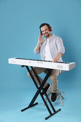 Smiling man playing synthesizer on light blue background