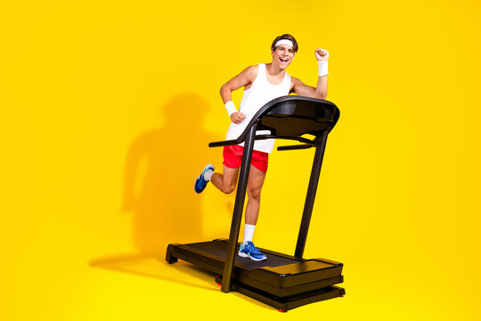 Energetic young man exercising on treadmill against a bright yellow background, wearing vibrant activewear and a headband.
