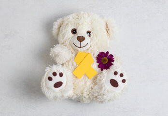 Yellow ribbon, teddy bear toy and gerbera flower on stone background.