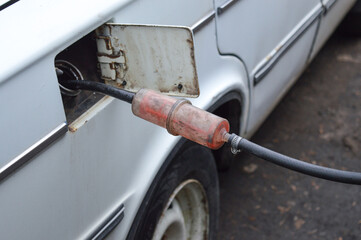 siphoning fuel from an old white car into a transparent plastic bottle black hose fuel tank...