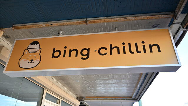 Yellow sign hanging outside bing chillin bingsu store, or ice cream shop, featuring the chain's cute Shiba Inu logo