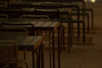 In a dimly lit environment, you can see empty tables meticulously arranged in neat rows, creating a...