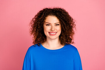 Young woman in a blue sweatshirt smiles against pink background, showcasing casual style and vibrant confidence.