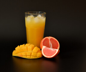 Fruit juice with ice on a black background, next to pieces of ripe mango and grapefruit.