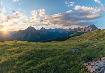 Fototapeta premium Beautiful summer landscape with green grass on the mountain top at sunset. Mountain range in the background, blue sky and clouds. Beautiful nature scene with sunlight. Beauty of the natural world.