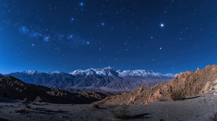 A panoramic night view of snow-capped mountains under a starry sky.