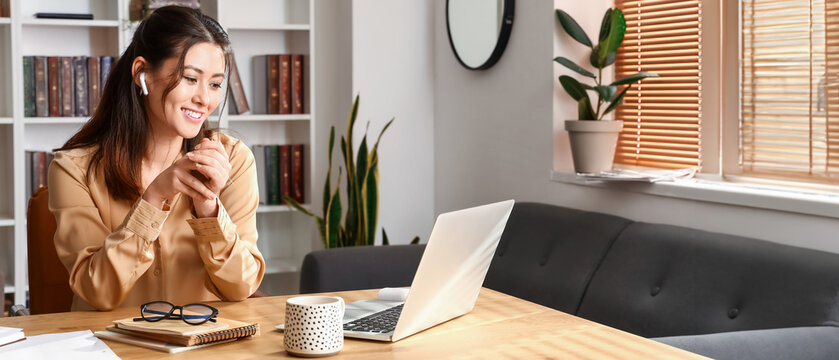 Young Asian tutor in earphones sitting at home