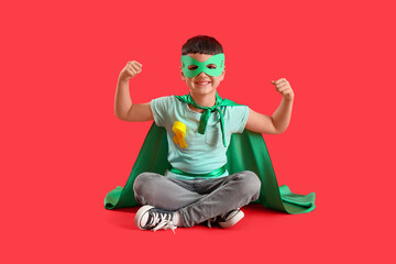 Little boy dressed as superhero with gold ribbon showing muscles on red background. Childhood cancer awareness concept
