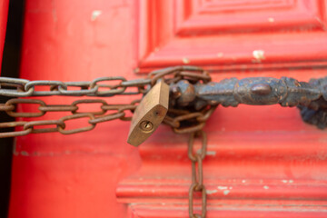 Closeup of metallic chains and locks in handles on red closed vintage doors. Full frame shot of vibrant wooden entrance outdoors. 