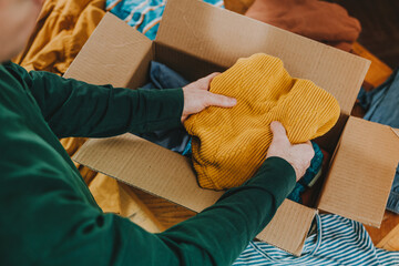 Unrecognizable man putting old clothes into box for charity or upcycling