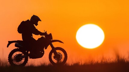 A motorcyclist navigates a path during sunset, silhouetted by the brilliant orange and yellow hues of the sky, showcasing freedom and adventure