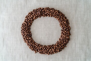 Obraz premium A circle of roasted coffee beans on a beige linen fabric, creating a visually appealing frame.