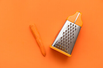 Metal grater and carrot on orange background