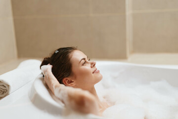 Relaxed young woman enjoying a bubble bath, smiling peacefully with her eyes closed. Self-care and wellness concept in a cozy bathroom setting.