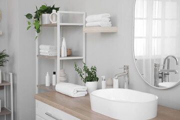 Folded clean towels with houseplants and cosmetic products on table in bathroom