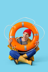 Male sailor with rescue ring sitting on blue background