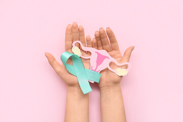 Female hands with turquoise ribbon and paper uterus on pink background. Cervical Health Awareness Month