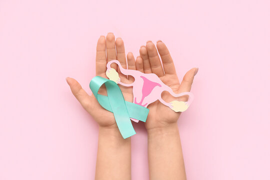 Female hands with turquoise ribbon and paper uterus on pink background. Cervical Health Awareness Month