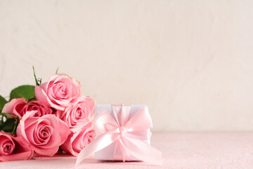 Pink roses with gift box on table against white background, closeup. Valentine's Day celebration