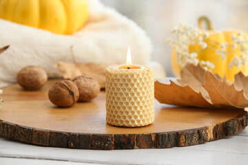 Burning candle with autumn leaves and nuts on board near window, closeup