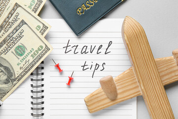 Notebook with text TRAVEL TIPS, wooden airplane and money on light background, closeup. Itinerary...