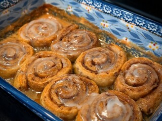 Delicious cinnamon rolls fresh from the oven topped with sweet icing glaze. Captured in a ceramic baking dish, these treats evoke warmth, comfort, and the joy of home baking moments.