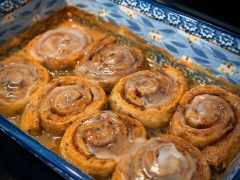 Delicious cinnamon rolls fresh from the oven topped with sweet icing glaze. Captured in a ceramic baking dish, these treats evoke warmth, comfort, and the joy of home baking moments.