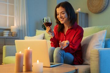Young woman with glass of wine having online date at home in evening