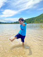 Happy boy playing in a crystal clear lagoon next to the sea with mountains and tropical vegetation of the Atlantic forest in the background in harmony with green and blue. Summer and joy