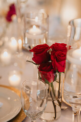 Elegant Red Roses in a Glass Vase with Candlelit Glow on a Formal Wedding Reception Table Setting