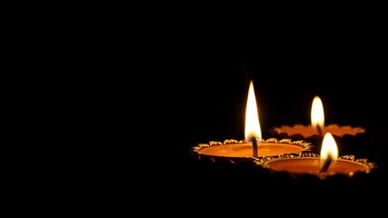 Close-up of intricate carved diya oil lamp with bright flame on dark background, light, glowing