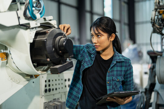 Focused female engineer analyzing a robotic system using a tablet in an advanced industrial factory.